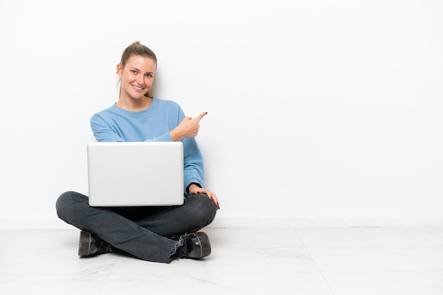 Jovem mulher com um laptop sentado no chão apontando para trás