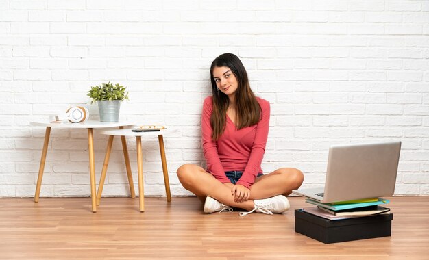 Jovem mulher com um laptop sentado no chão dentro de casa. Retrato