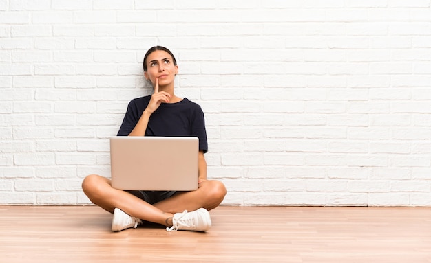 Jovem mulher com um laptop sentado no chão pensando uma idéia