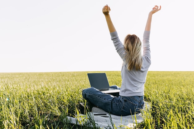 Jovem mulher com um laptop trabalhando, sentado em campo com grama verde fresca.