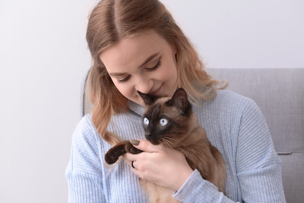 Jovem mulher com um lindo gato tailandês sentado na poltrona