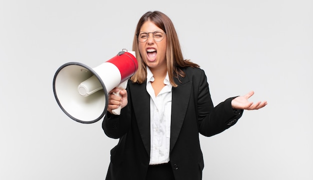 Jovem mulher com um megafone parecendo zangada, irritada e frustrada gritando wtf ou o que há de errado com você