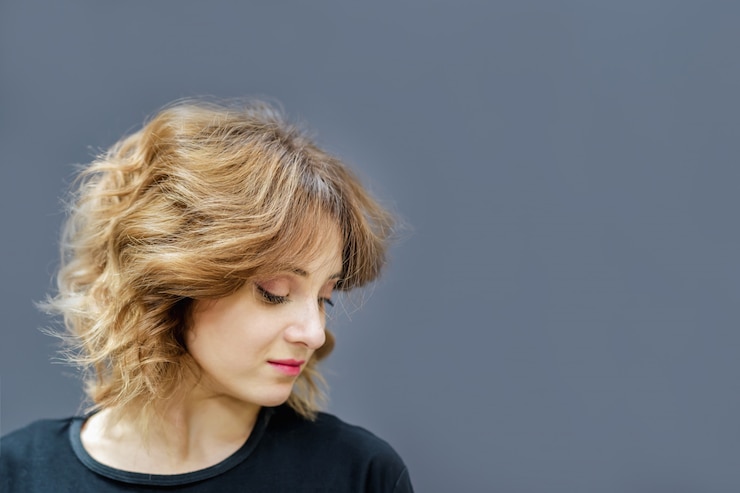Foto jovem mulher com um penteado encaracolado na parede cinza
