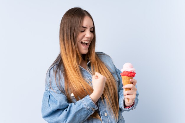 Jovem mulher com um sorvete de corneta isolado na parede azul comemorando uma vitória