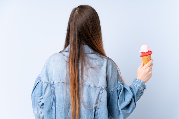 Jovem mulher com um sorvete de corneta na parede azul em posição traseira