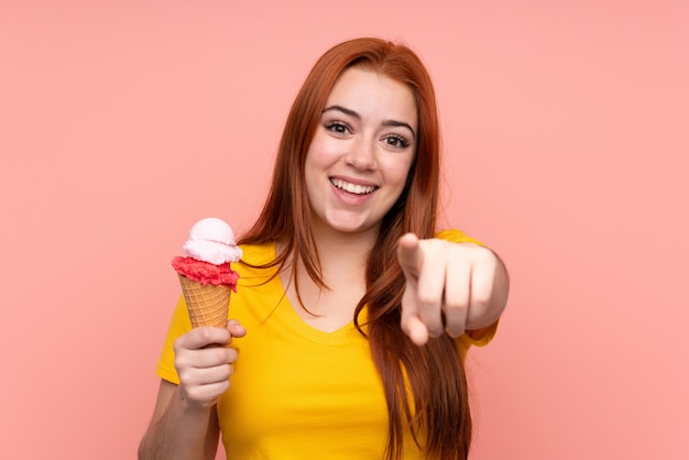Jovem mulher com um sorvete de corneta sobre parede isolada aponta o dedo para você com uma expressão confiante