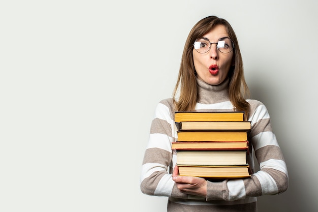 Jovem mulher com um suéter e óculos, segurando uma pilha de livros