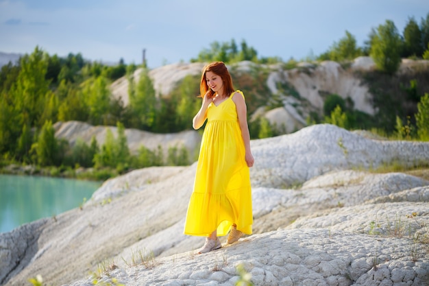 Jovem mulher com um vestido amarelo perto do lago com água azul e árvores verdes.