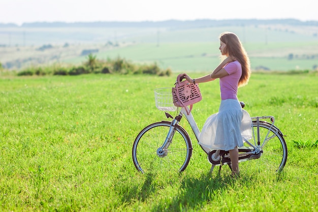Jovem mulher com uma bicicleta no campo verde em um dia ensolarado