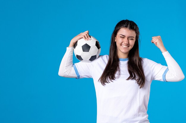 Jovem mulher com uma bola de futebol na parede azul de frente