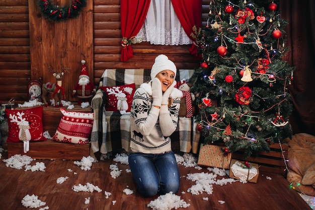 jovem mulher com uma camisola e um chapéu em casa perto da árvore de Natal