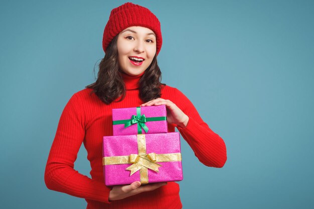 Jovem mulher com uma camisola vermelha e um boné com um presente de Natal. Sobre um fundo azul.