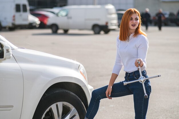 Jovem mulher com uma chave inglesa esperando ajuda para trocar a roda de um carro quebrado