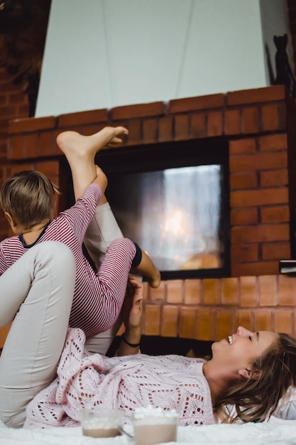 Jovem mulher com uma criança. mãe e filho estão brincando, se divertindo perto da lareira.