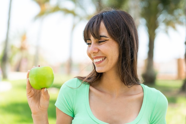 Jovem mulher com uma maçã ao ar livre com expressão feliz