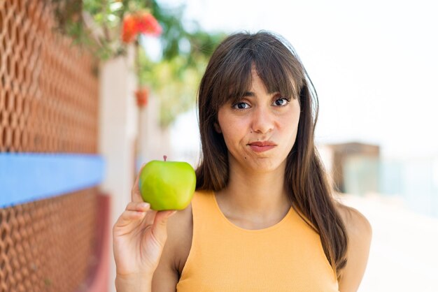 Jovem mulher com uma maçã ao ar livre com expressão triste