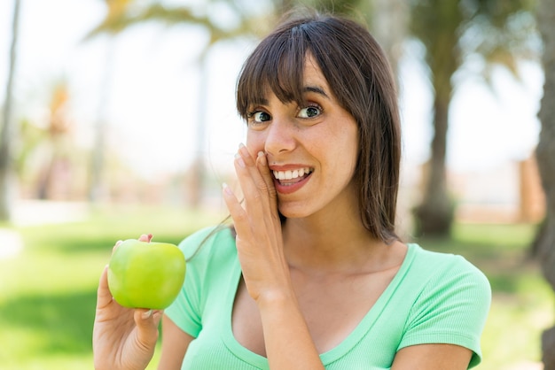Jovem mulher com uma maçã ao ar livre sussurrando algo