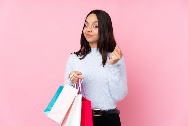 Jovem mulher com uma sacola de compras sobre parede rosa isolada, fazendo gesto de dinheiro