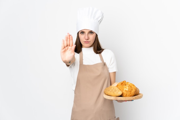 Jovem mulher com uniforme de chef na parede branca, fazendo o gesto de parada com a mão