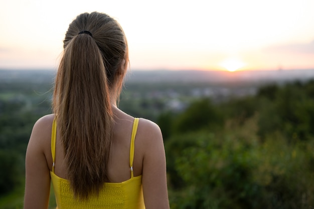 Foto jovem mulher com vestido de verão em pé ao ar livre, aproveitando o dia quente.