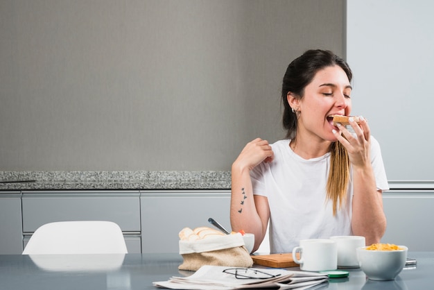 Foto jovem mulher comendo o pão no café da manhã