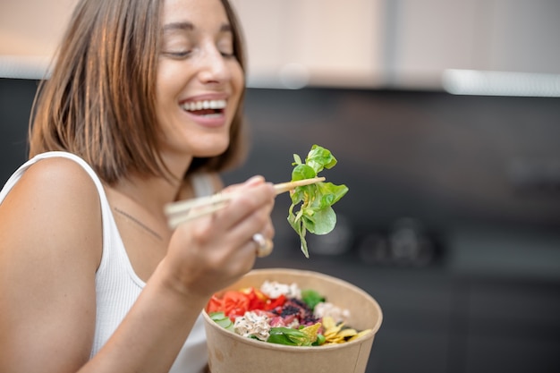 Jovem mulher comendo tigela asiática saudável com atum e salada na cozinha moderna em casa. Comida asiática para levar saudável e estilo de vida moderno em casa