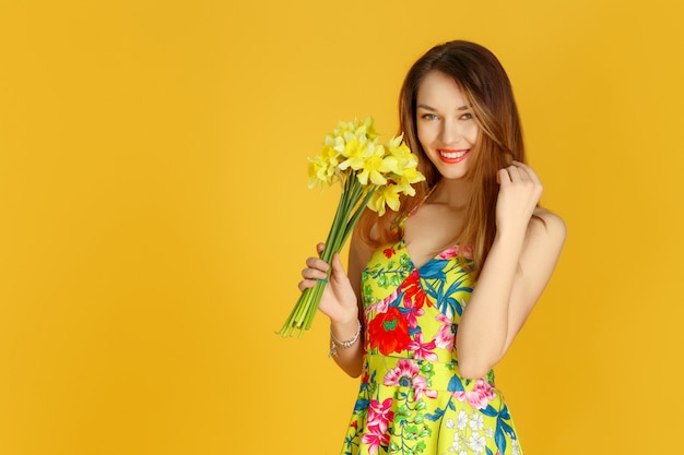 Jovem mulher contra parede amarela com flores na mão