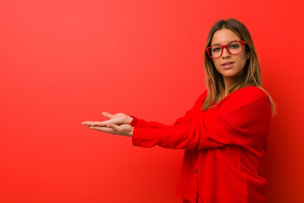 Foto jovem mulher contra uma parede, segurando um espaço de cópia em uma palma.