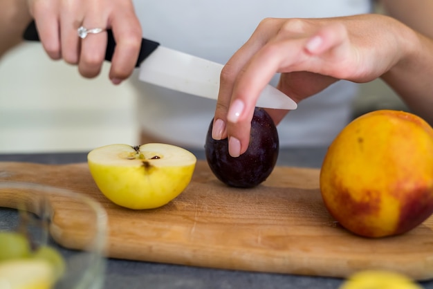 Foto jovem mulher cortando frutas diferentes, cozinhar alimentos saudáveis em uma mesa de madeira kitche. preparando pratos