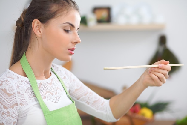 Jovem mulher cozinhando em uma cozinha Dona de casa saboreando sopa com colher de pau