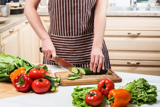 Jovem mulher cozinhando na cozinha em casa. Comida saudável. Dieta. Conceito de dieta. Estilo de vida saudável. Cozinhando em casa. Preparar comida. Uma mulher corta um pepino e legumes com uma faca.