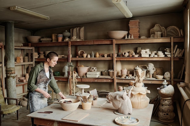 Jovem mulher criando esculturas de cerâmica com argila na mesa da oficina