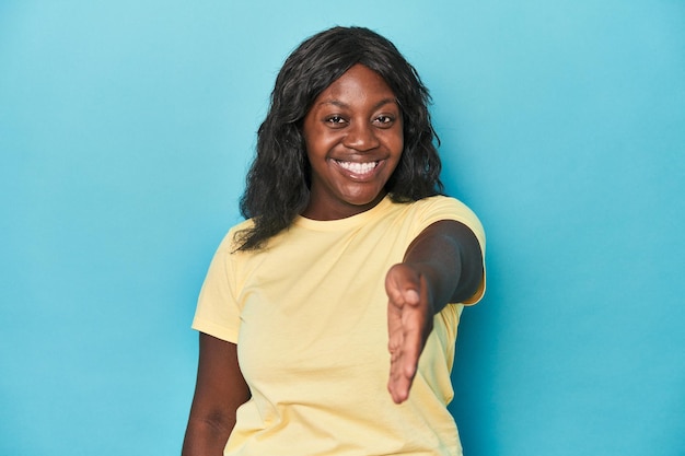 Jovem mulher curvilínea afro-americana esticando a mão para a câmera em gesto de saudação