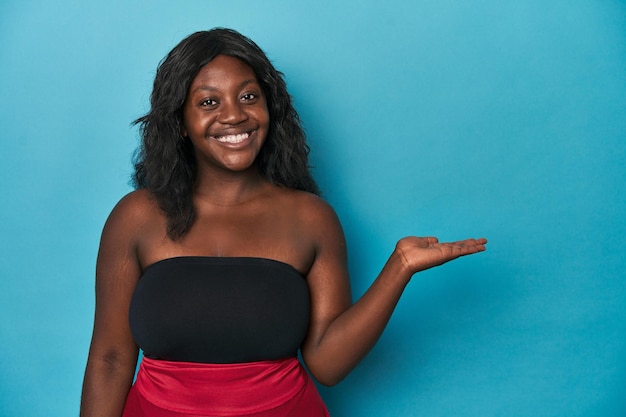 Jovem mulher curvilínea afro-americana mostrando um espaço de cópia na palma da mão e segurando a outra mão na cintura