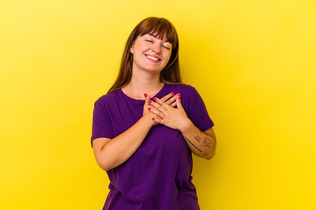 Jovem mulher curvilínea caucasiana isolada em fundo amarelo tem uma expressão amigável, pressionando a palma da mão no peito. Conceito de amor.