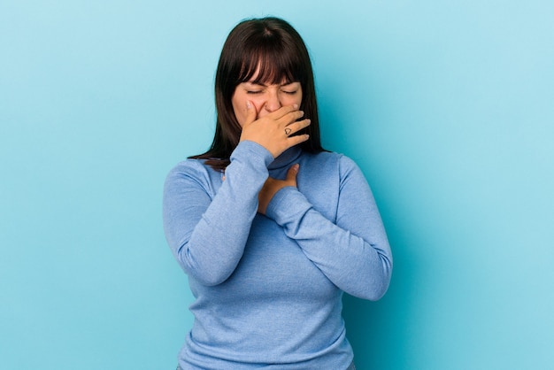 Jovem mulher curvilínea caucasiana, isolada em um fundo azul, sofre de dor na garganta devido a um vírus ou infecção.