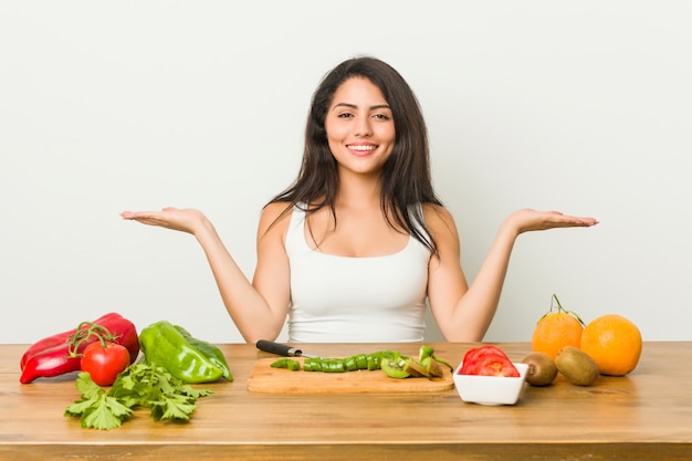 Jovem mulher curvilínea preparando uma refeição saudável faz escala com os braços, sente-se feliz e confiante.