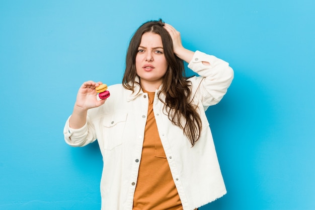 Jovem mulher curvilínea segurando macaroons em choque, ela se lembrou de um encontro importante.