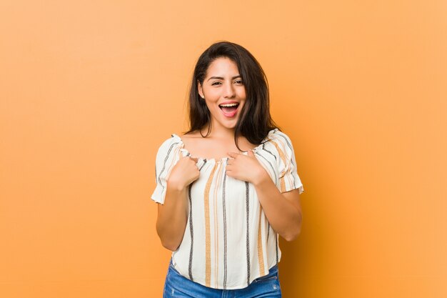 Jovem mulher curvilínea surpreendeu apontando com o dedo, sorrindo amplamente