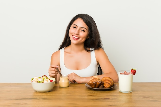 Jovem mulher curvilínea tomando um café da manhã feliz, sorridente e alegre.