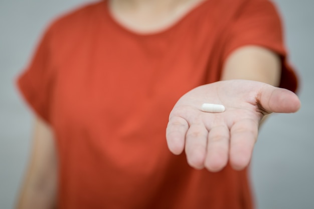 Jovem mulher dando comprimidos de uma cápsula branca na mão.