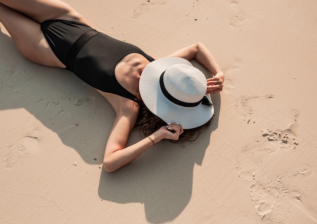 Jovem mulher de biquíni preto de luxo, deitado na areia da praia tropical