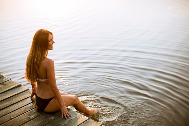 Jovem mulher de biquíni, sentado em um píer no lago