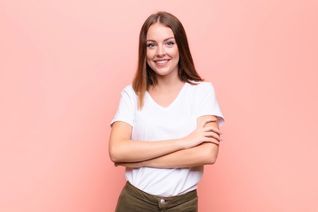 Jovem mulher de cabeça vermelha, parecendo um empreendedor feliz, orgulhoso e satisfeito, sorrindo com os braços cruzados contra a parede plana