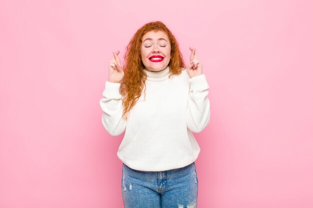 Jovem mulher de cabeça vermelha sorrindo e cruzando ansiosamente os dois dedos