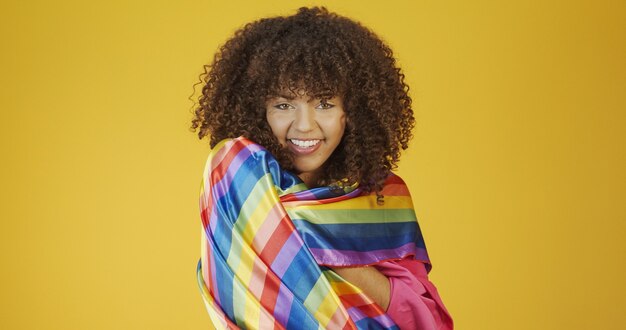 Jovem mulher de cabelo encaracolado cobrindo a bandeira do orgulho lgbt com o punho erguido cobrindo a bandeira lgbt