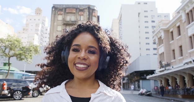 Foto jovem mulher de cabelos cacheados e fones de ouvido correndo na rua.