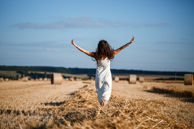 Jovem mulher de cabelos cacheados em um campo de trigo, onde há um enorme feixe de feno, curtindo a natureza. pessoas e viagens. natureza. raios de sol agricultura