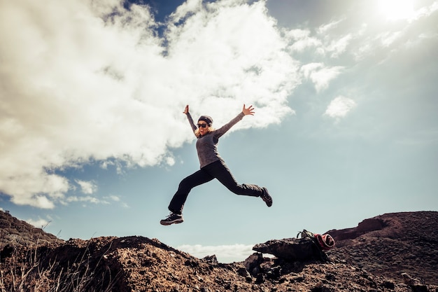 Jovem mulher de meia-idade pula para as pedras pelo conceito de felicidade e sucesso durante uma viagem de trekking turístico - conceito de liberdade e pessoas modernas em atividades de lazer ao ar livre