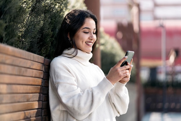 Jovem mulher de negócios digitando em seu telefone. Ela está sorrindo e vestindo roupas casuais elegantes